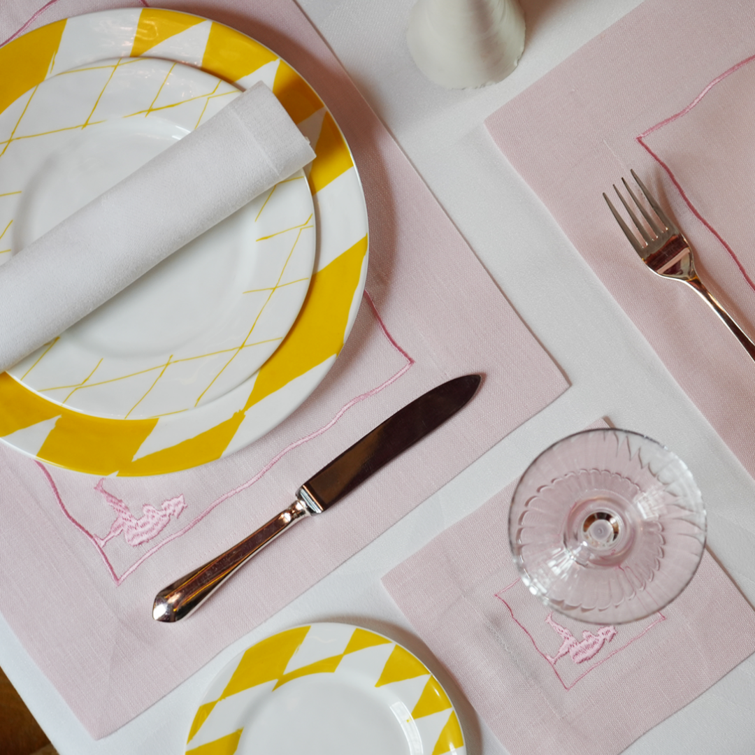Load image into Gallery viewer, Dining table setting with yellow and white plates, pink placemats, and cutlery.