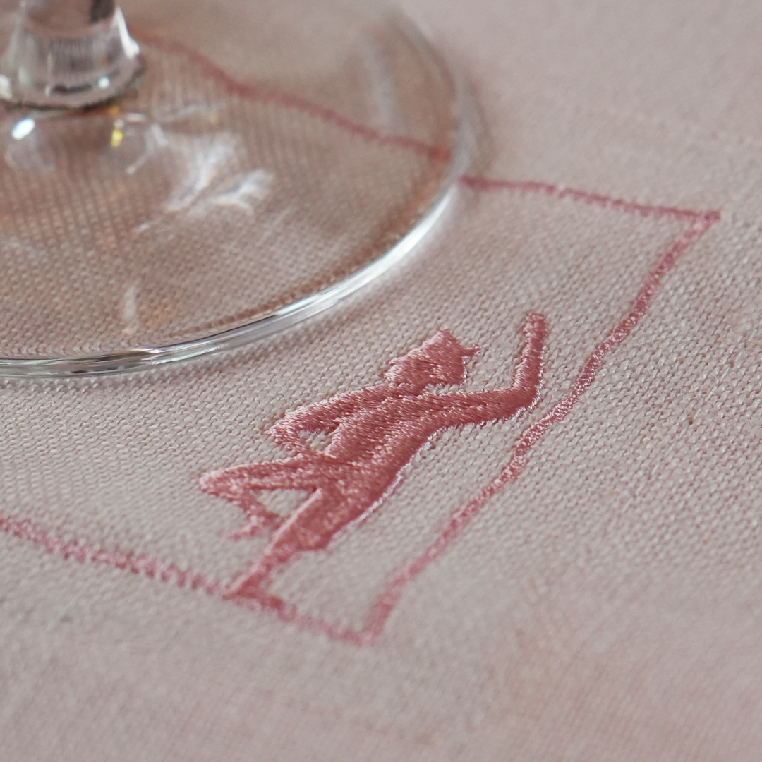 Load image into Gallery viewer, Embroidered design of a person climbing a mountain on a fabric surface with a glass object.