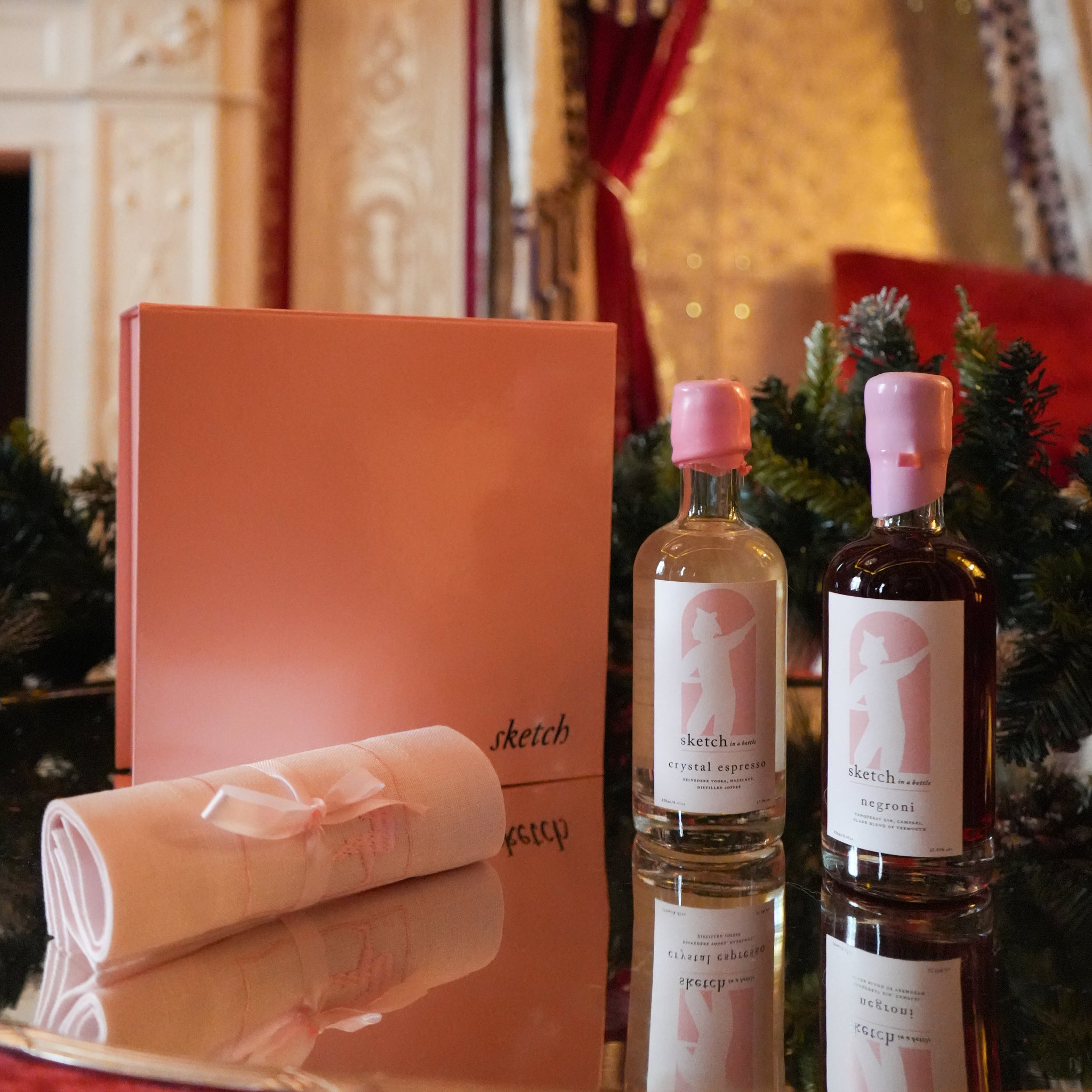 Load image into Gallery viewer, Two bottles of 'sketch' alcohol with a pink box and gift wrap on a reflective surface.